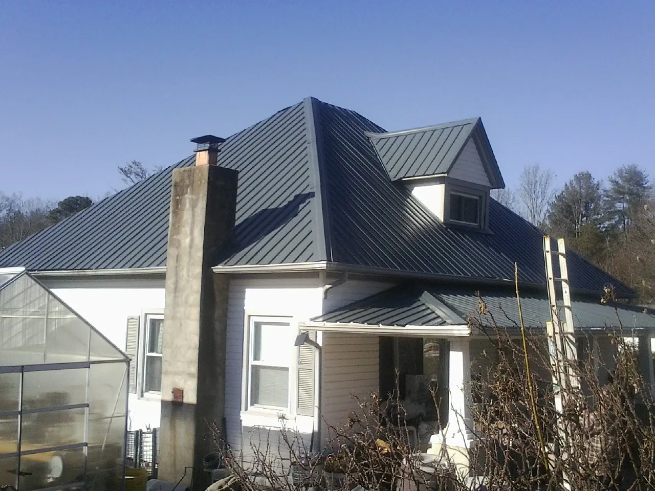 Dark blue standing seam metal roof on a white farmhouse with dormer — Slate & Tile Roof Repair by Roofing Brothers in Beachwood