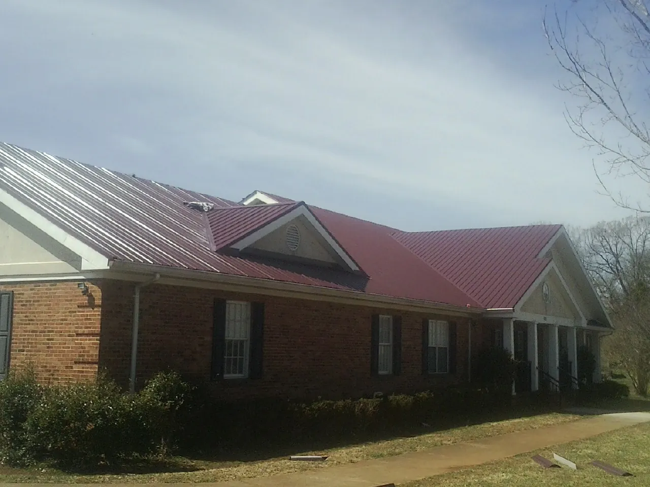 Red metal roof with gabled entries on a long brick building, from a Hail Damage Roof Repair job in Beachwood