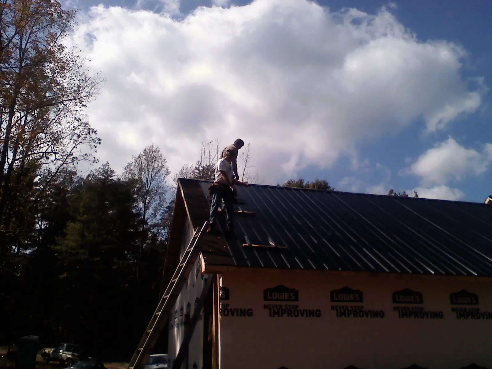 Roofer fastening dark metal panels high against a cloudy sky, from a Roof Inspection job in Beachwood